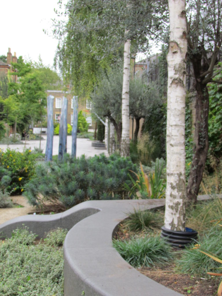 A shared road in Lambeth with blue/grey stone, beautiful tall trees, low walls and stepping stones for children in Van Gogh Walk