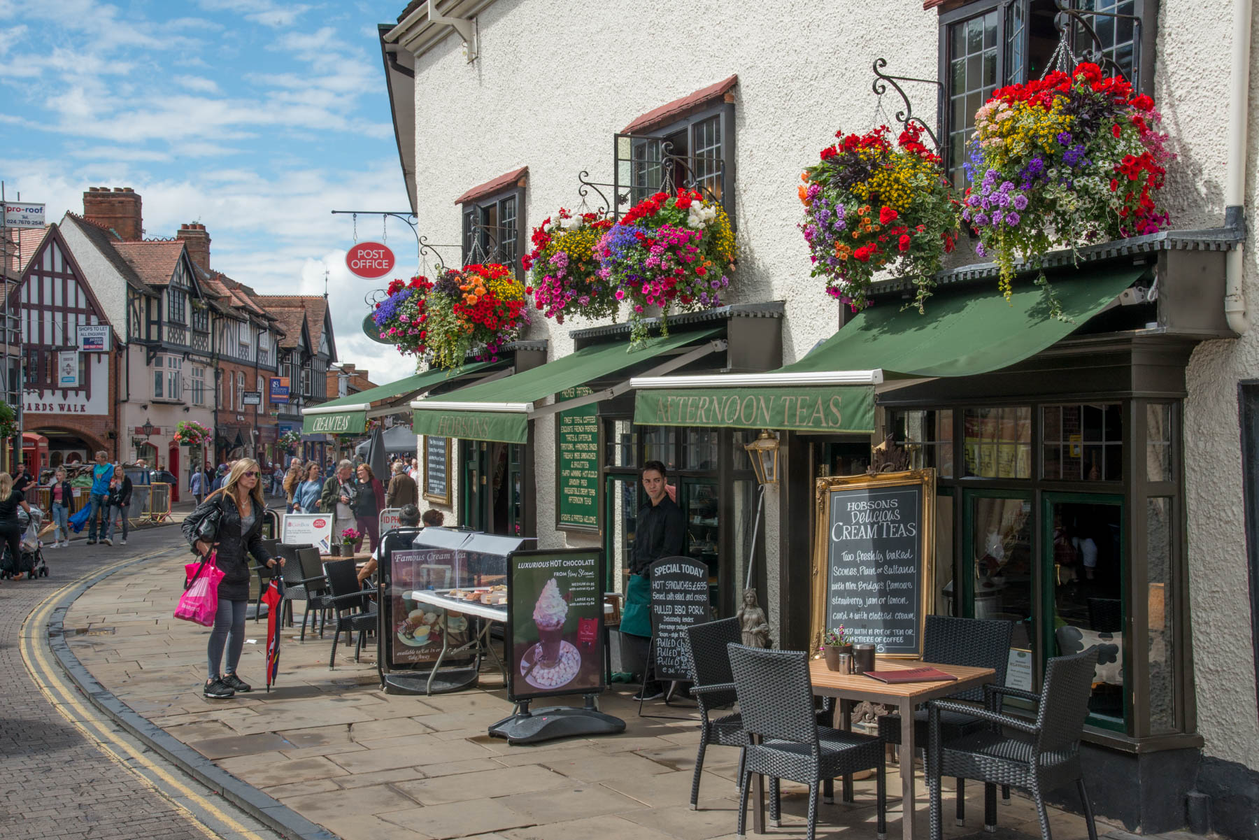 A prety shopping street in Stratford with seats outside cafes and large hanging baskets of flowers.